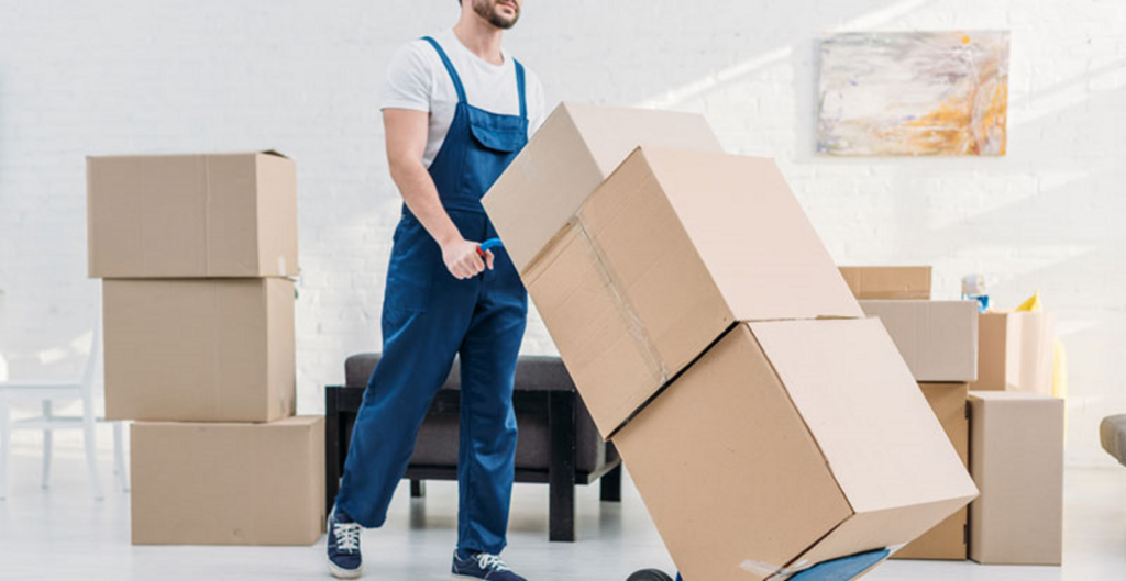 Mover in overalls stacking cardboard boxes while packing a room